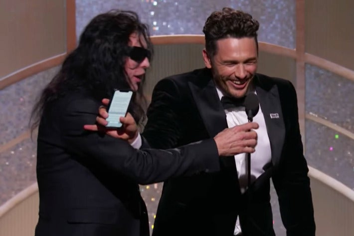 Tommy Wiseau, wearing sunglasses, reaches for the microphone while James Franco, laughing, blocks his arm